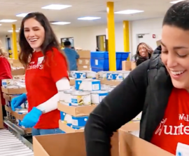People stand alongside a conveyor belt as they load supplies into donation boxes.