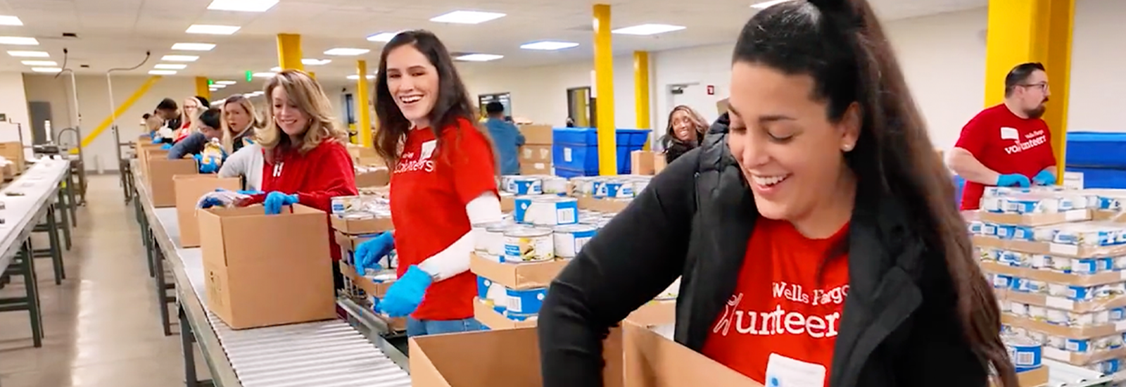 People stand alongside a conveyor belt as they load supplies into donation boxes.