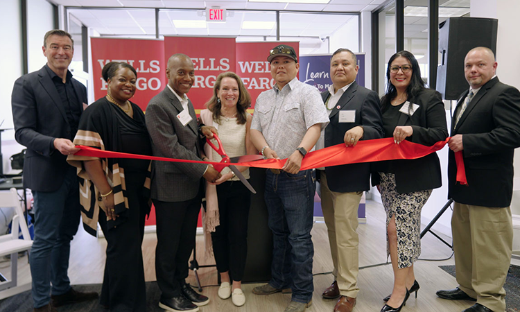 Several people stand behind a ribbon as the person near the center cuts the ribbon. 