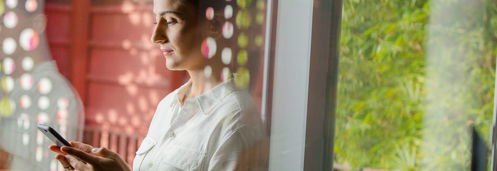 A woman is looking down at a cell phone that she is holding with both hands.