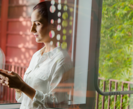 A woman is looking down at a cell phone that she is holding with both hands.