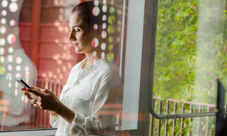 A woman is looking down at a cell phone that she is holding with both hands.