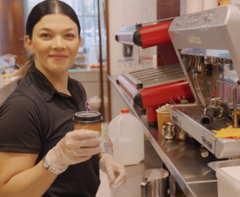 A woman in a smoothie bar is holding a cup with a lid and smiling.