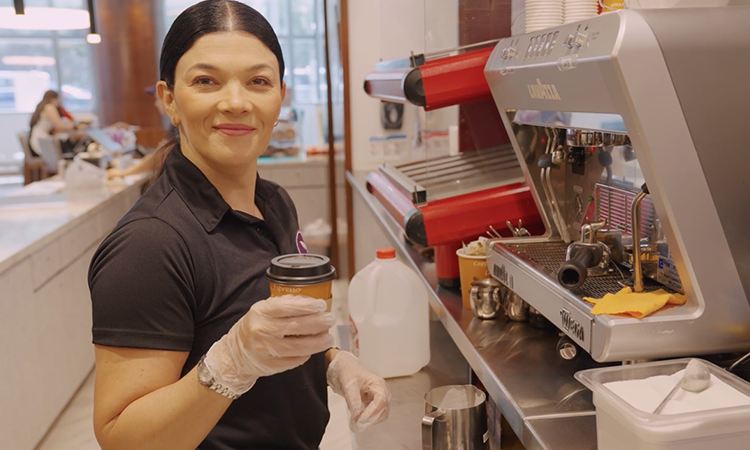 A woman in a smoothie bar is holding a cup with a lid and smiling.