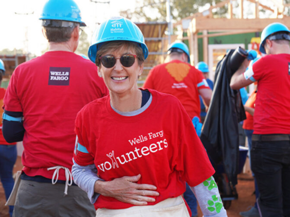 A woman in a red volunteer shirt and blue construction hat smiles for a picture at a construction site.