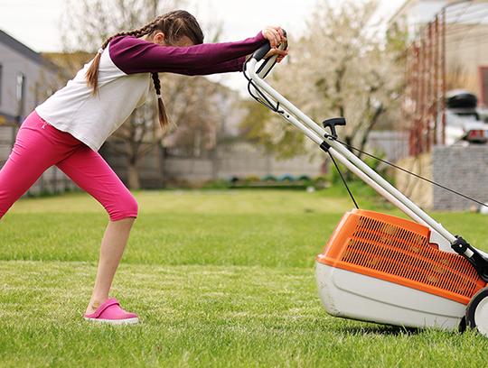 A teen pushes a lawn mower over a lawn of green grass.