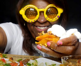 A person wearing yellow rimmed glasses holds a tiny taco.