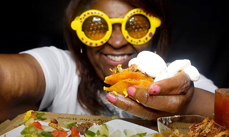 A person wearing yellow rimmed glasses holds a tiny taco.
