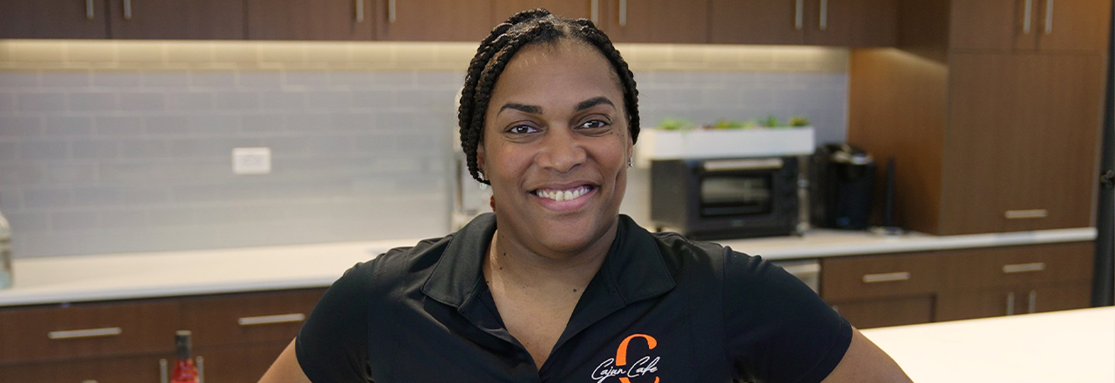 A woman in a black shirt with orange lettering stands in a kitchen