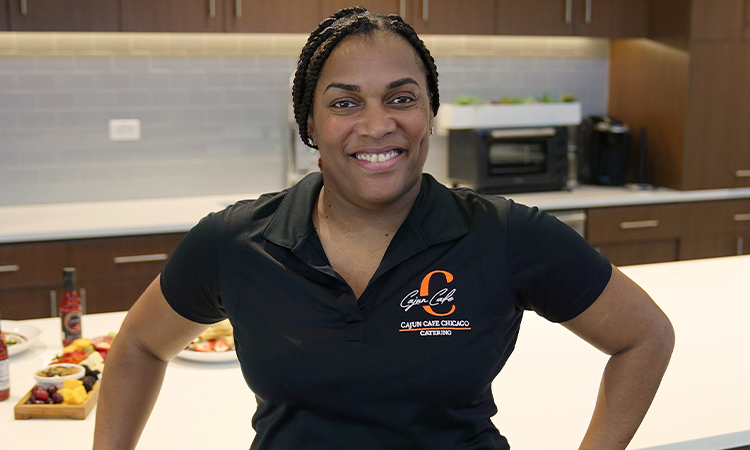 A woman in a black shirt with orange lettering stands in a kitchen