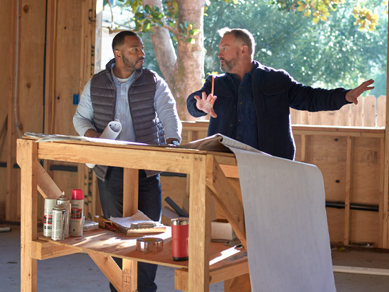 Two men talk to each other while discussing blueprints.