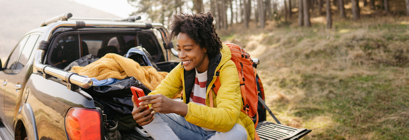 A woman sits in the cargo bed of a pickup truck, looking at a smartphone.