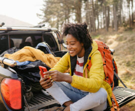 A woman sits in the cargo bed of a pickup truck, looking at a smartphone.