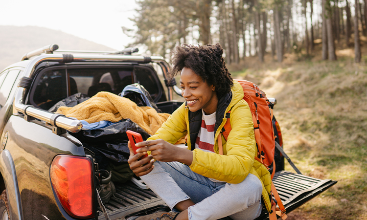 A woman sits in the cargo bed of a pickup truck, looking at a smartphone.