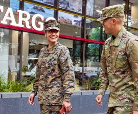 Two soldiers - a woman and a man - smile at each other while they walk past a Wells Fargo branch
