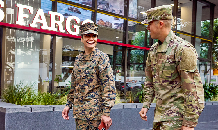 Two soldiers - a woman and a man - smile at each other while they walk past a Wells Fargo branch