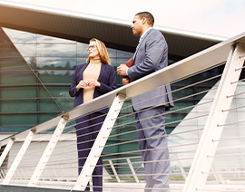A man and woman stand in business attire in front of a railinf