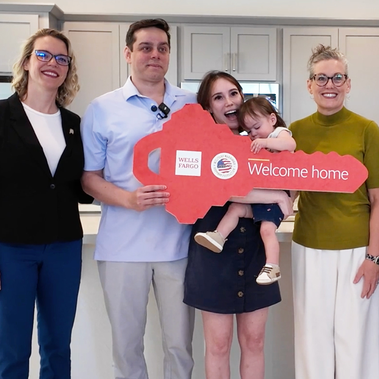 A family stands in front of their new home holding an oversized key that says "Welcome Home"