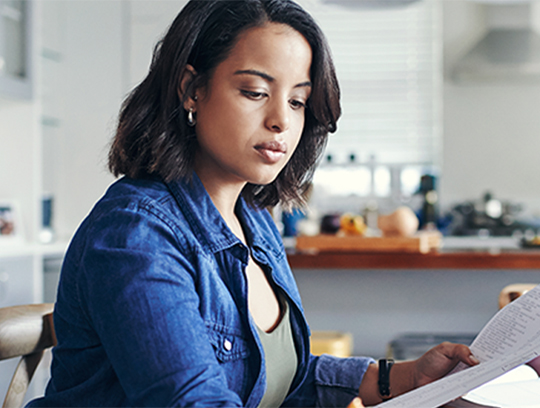 A woman in a blue denim shirt is looking down at a piece of paper in her hands.
