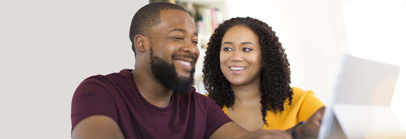 A man and woman smile at each other while looking at a tablet screen.
