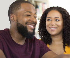 A man and woman smile at each other while looking at a tablet screen.