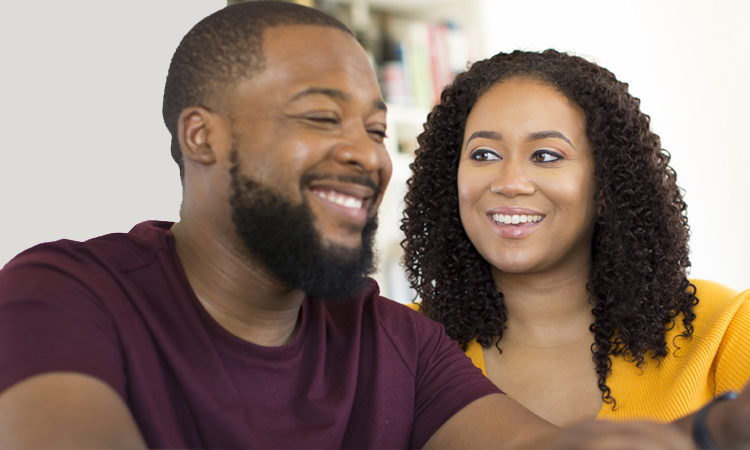 A man and woman smile at each other while looking at a tablet screen.