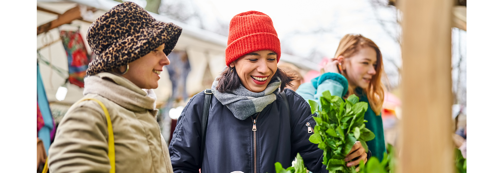 Three women dressed for winter in jackets, scarves, and hats are smiling while outside.