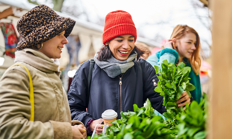 Three women dressed for winter in jackets, scarves, and hats are smiling while outside.