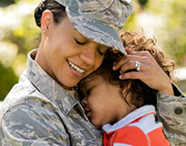 A woman in camouflaged military attire is hugging a young child.