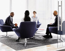 A group of people sit in chairs in an office setting having a conversation.