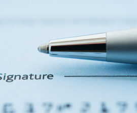 A ballpoint pen rests on a piece of paper above the word Signature