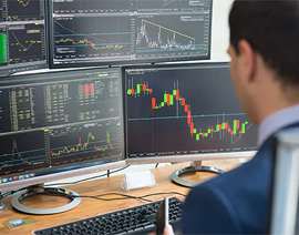A person is seen from behind looking at graphs on multiple computer screens.
