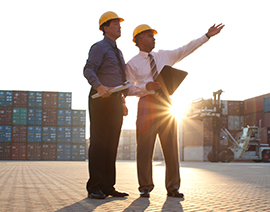 Two men in hard hats and dress clothes on a site, pointing.