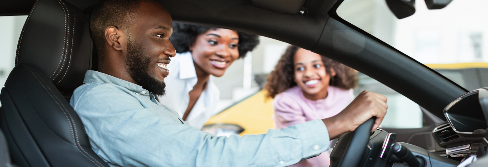 A man sits in a car as his wife and daughter look through the driver’s side window