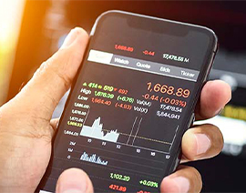 A close-up shot of a hand holding a phone displaying stock market information.