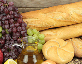 A table displaying bread, grapes, and some sort of liquid.
