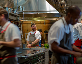 People wearing aprons working in a kitchen.