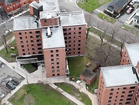 An aerial view of an apartment complex. The buildings are brick and surrounded by grass.