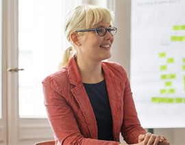 A woman wearing glasses is smiling and looking at a computer offscreen.