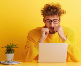A man sitting at a desk appears to be stressed as he looks at his laptop.