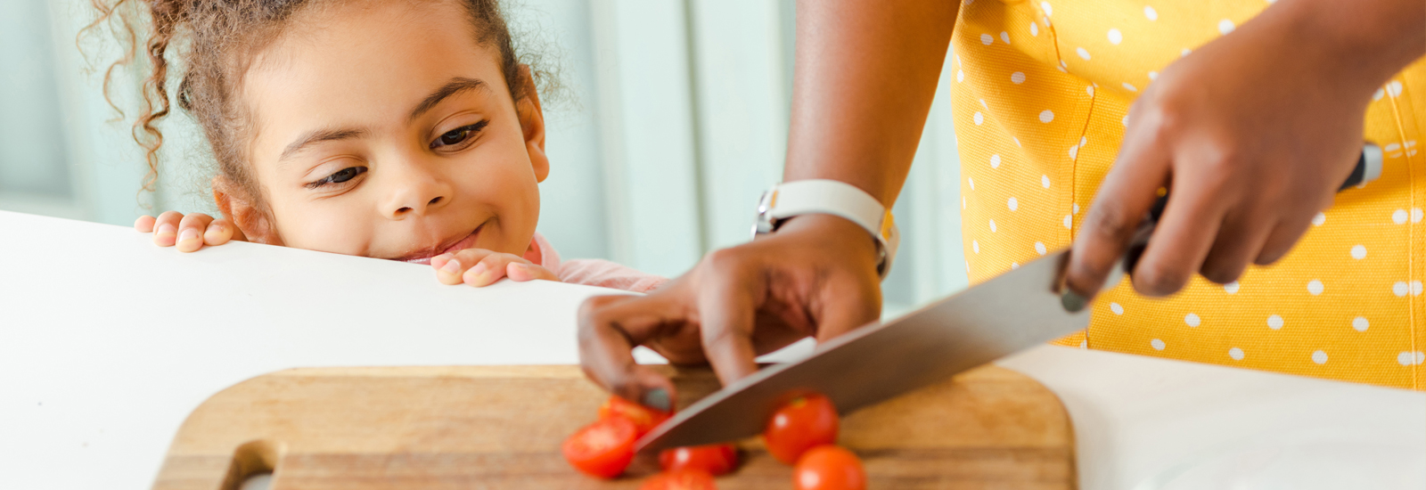 A young child watches as her parent cuts tomatoes.