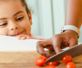 A young child watches as her parent cuts tomatoes.