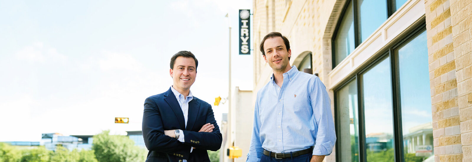 Two people stand outside a brick office building with an Irys sign visible in the background.