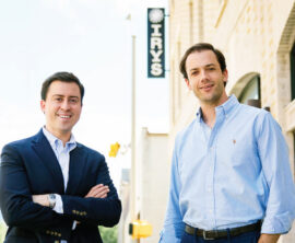 Two people stand outside a brick office building with an Irys sign visible in the background.