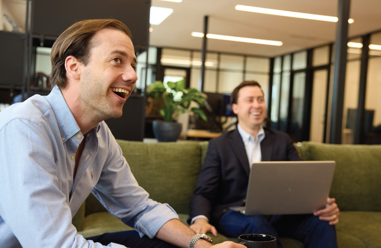 Two people sit in a modern office lounge area, with a laptop open during a discussion.