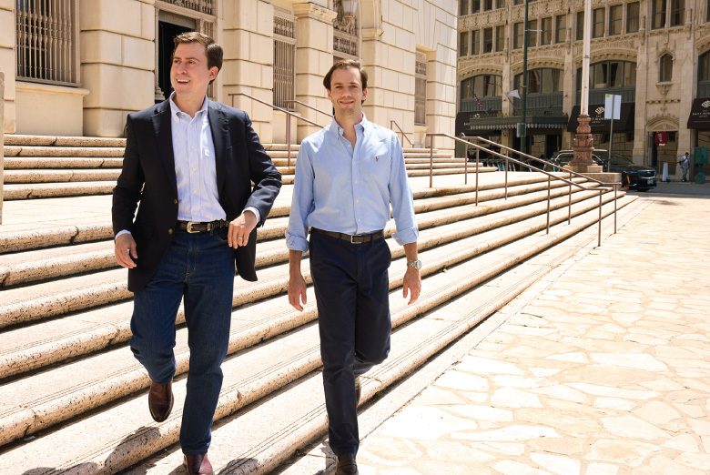 Two people in business attire walk down stone steps outside an office building in downtown San Antonio.