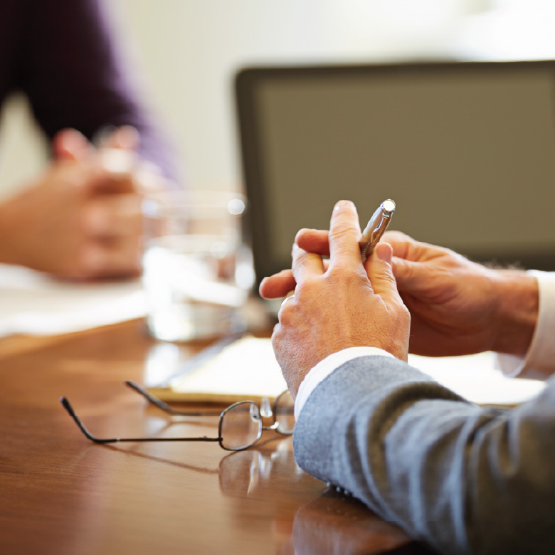 Close-up of a person holding a pen during a meeting at a table.