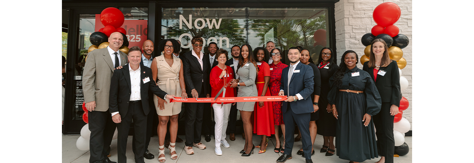 A group of community leaders and Wells Fargo representatives stand outside a branch during a ribbon-cutting ceremony.