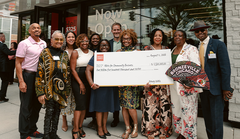 Community members pose outside a Wells Fargo branch while holding a ceremonial grant check.