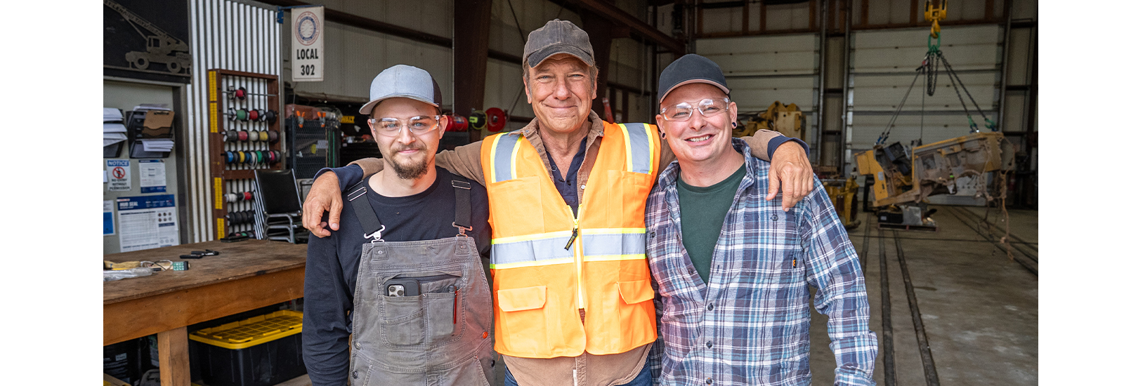 Three smiling men stand together in a workshop